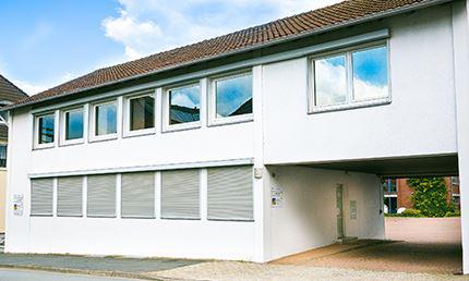 Außenansicht des Beratungsgebäudes der AWO mit heller Fassade und moderner Fensterfront. gebäude, beratungshaus, außenansicht, weißes-haus, fensterfront, zweigeschossig,